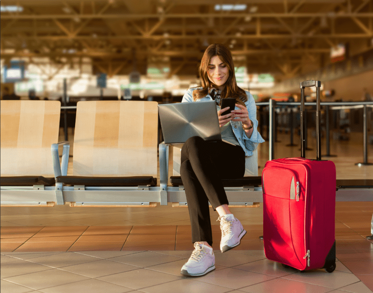 Woman sitting with laptop, suitcase and phone in an airport