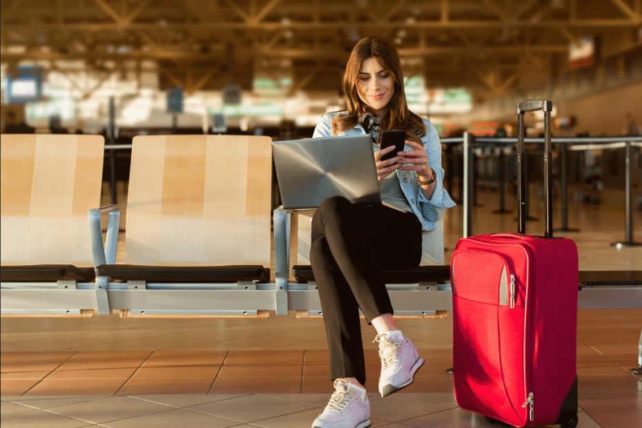 Woman sitting with laptop, suitcase and phone in an airport