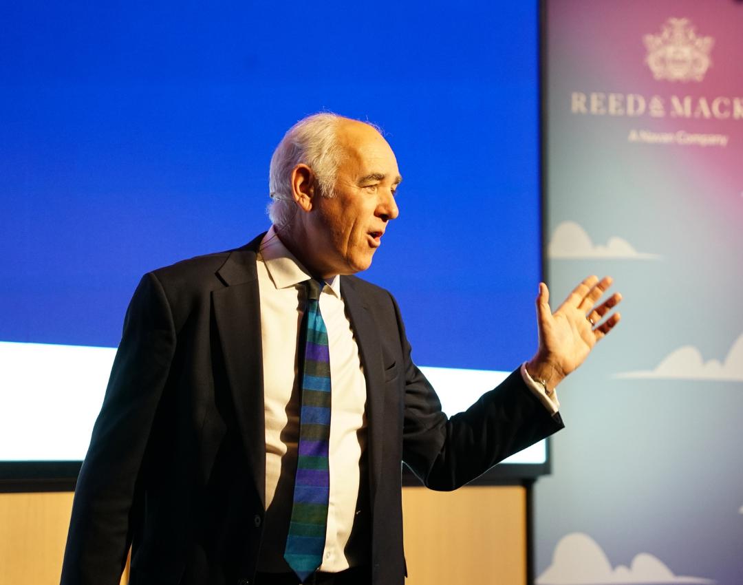 Speaker at a conference in front of a digital screen